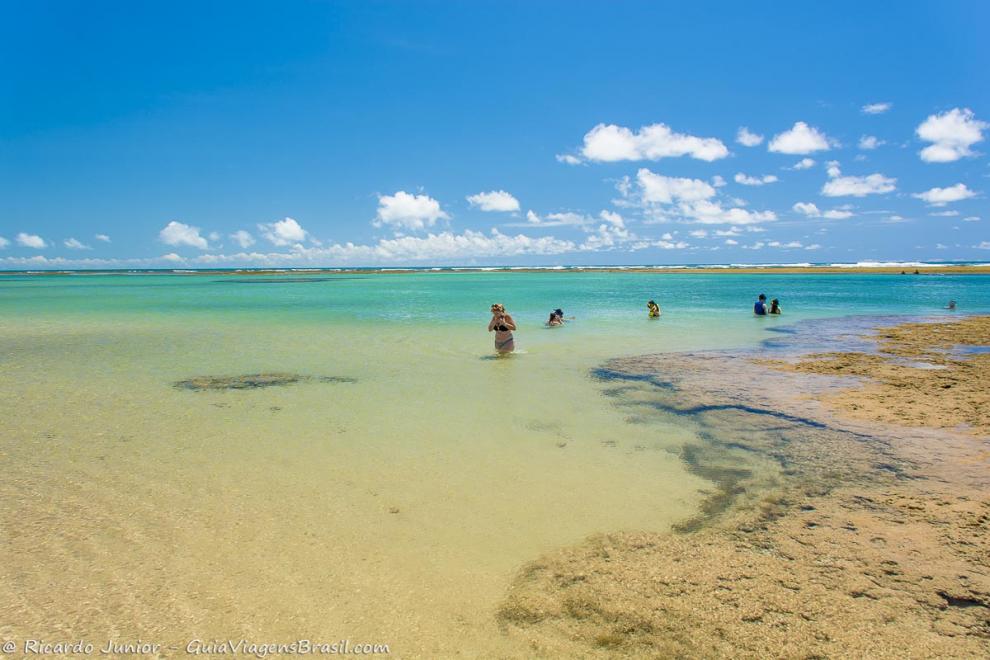 Imagem de turistas no mar azulado da Praia Taipu de Fora.